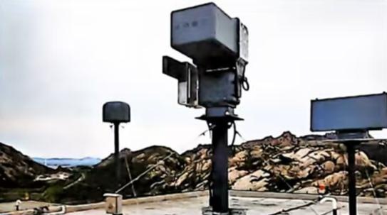 户外山地场景中的立柱式低空监测设备，旁有天线及控制屏